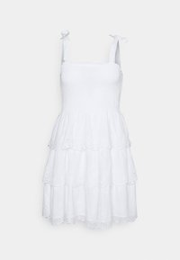 Bílá bezramínková sluneční šaty s vázacími ramínky, smockovaným živůtkem a vrstvenou sukní, která má krajkový vzor a zvlněné okraje.