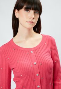 Rosa gerippter Cardigan mit floralen Verzierungen und silbernen Akzenten, rundem Ausschnitt und langen Ärmeln. Glatte Textur und taillierte Passform.