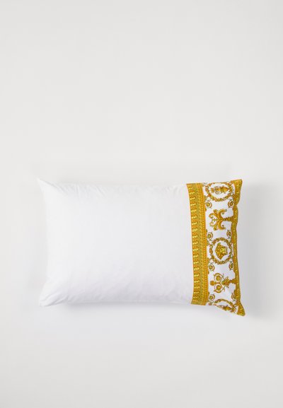 Hvit pute med en dekorativ gul mønstret kant langs en kant, som har intrikate design og en glatt tekstur.