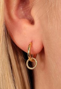 Guldörhängen med en slät, snodd design. Den större ringen fästs vid en mindre, texturerad ring, vilket framhäver kontrasterande ytor.