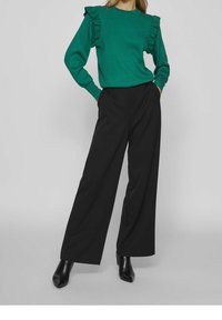 Grön ribbade tröja med volangärmar, ihop med svarta vida byxor. Outfit kompletteras med svarta spetsiga stövlar.