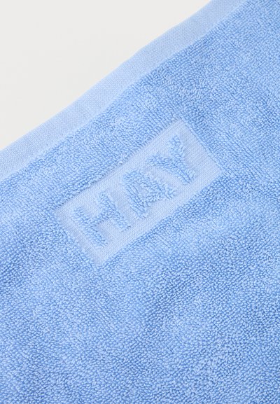 Svetlo modra brisača iz frote z besedo "HAY" v izbočeni tkanini blizu roba na belem ozadju.