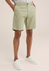 Svetlozelené bavlnené šortky s plochým predným dielom, bočnými vreckami a zapínaním na gombík, skombinované s bielymi teniskami. Hladká textúra a ležérny dizajn.