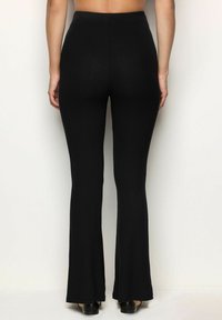 Zwarte geribde flared broeken met een elastische tailleband, een gladde textuur en zacht uitbreidende benen tot op de vloer. Eenvoudig ontwerp, geen zichtbare hardware.