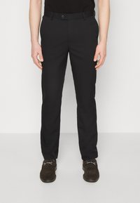 Pantalones negros de pierna recta, hechos de una tela suave. Cuentan con un cierre de botón y trabillas para cinturón. Llevados con mocasines marrones.