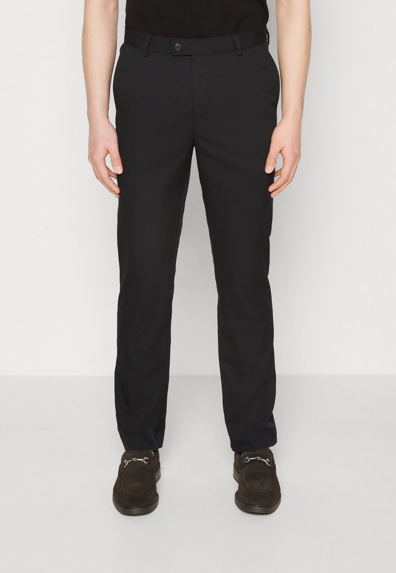 Black trousers with a straight leg, made of soft fabric. They feature a button closure and belt loops. Worn with brown loafers.