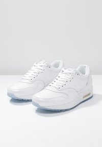 Vita atletiska sneakers med en slät läderöverdel, rund tå och synligt luftkudding i sulan. Snören i vitt, med en blå genomskinlig sula.