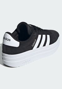 Czarne zamszowe sneakersy z trzema białymi paskami i białym akcentem na pięcie. Posiadają grubą białą platformę i czarne sznurowadła.