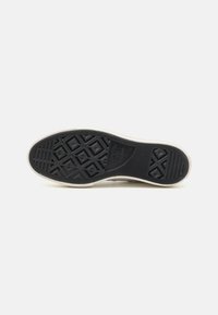Suela de zapato de goma negra con patrones de agarre texturizados, con un borde blanco. Incluye diseños en forma de diamante y estrella en la parte inferior.