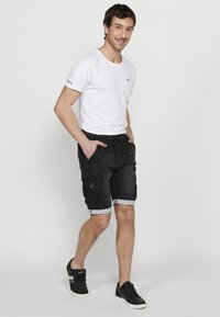 Pantalones cortos cargo de mezclilla negra con dobladillos enrollados, que cuentan con múltiples bolsillos y una cintura con cordón. Combinados con una camiseta blanca de manga corta lisa.