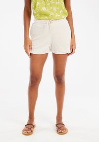Shorts beige clair en tissu doux avec une taille élastique et un cordon de serrage, assortis à des sandales brunes à lanières.