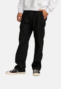 Zwarte denim jeans met een rechte pijp, contrasterende oranje stitching, voorzakken en gedragen met zwarte sneakers.