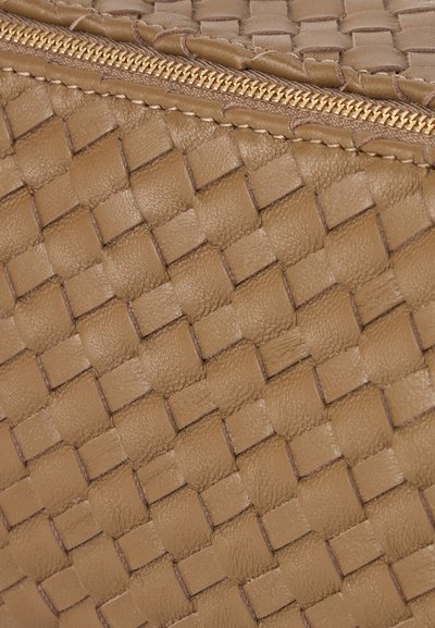 Gros plan sur une texture de cuir tanné tissé avec des coutures détaillées et une fermeture éclair dorée.