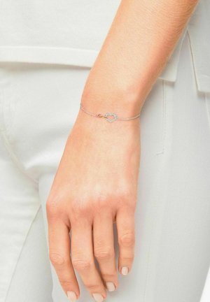Bracciale in argento con chiusura a forma di cuore decorata con piccoli gemme trasparenti. Indossato su una mano con smalto naturale.
