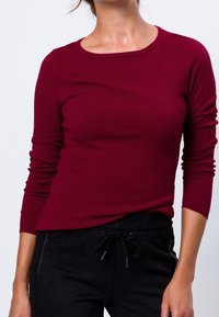 Chemise longue à manches longues texturée bordeaux avec un col rond, un design ajusté et des détails en côtelé. Associée à un pantalon noir à cordon de serrage.