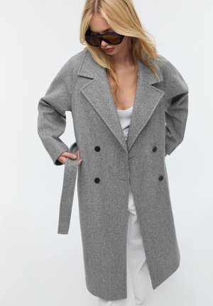 Manteau en laine gris à double boutonnage avec grands revers, boutons et ceinture à nouer. Doté de manches longues et d'une silhouette légèrement ample.