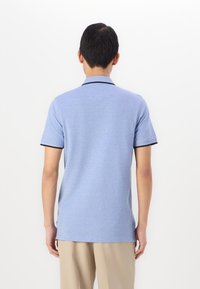 Light blue polo shirt with short sleeves, black collar trim, and a textured finish. Features a straight hem and side slits for ease of movement.