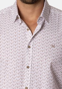 Camisa blanca de botones con un patrón repetido de hojas marrones, elaborada en una tela liviana, con botones marrones y un sutil logo en el pecho.