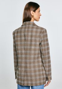 Hnědý kostkovaný blazer se strukturovaným designem, disponující klopovým límcem a zapínáním na knoflíky, vyrobený z texturované tkaniny.