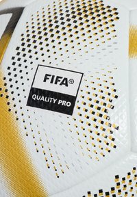 Vit fotboll med gyllene och svarta prickiga mönster. Innehåller FIFA-logotyp och etikett för "QUALITY PRO". Texturerad yta för bättre grepp.
