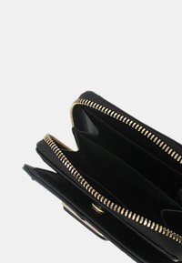 Portafoglio in pelle nera con cerniera dorata, dotato di molteplici scomparti e texture liscia. L'interno comprende fessure per carte e una tasca aperta.