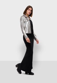 Veste cropped argent métallique avec un col, associée à une robe noire ajustée et des bottes à talons larges noires.