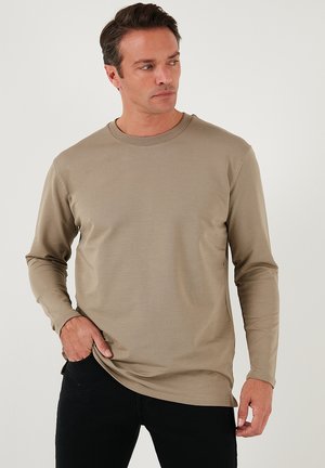 Long-sleeve beige shirt made of smooth fabric, featuring a round neck and a relaxed fit, paired with black pants.