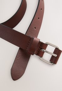 Cintura in pelle marrone con una texture liscia, caratterizzata da una fibbia in metallo argentato. La cintura presenta dei fori per la regolazione e una punta affusolata.