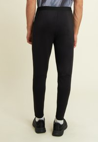 Pantalons de sport noirs avec une texture lisse, coupe ajustée et taille élastique, associés à des baskets noires et des chaussettes blanches à la cheville.