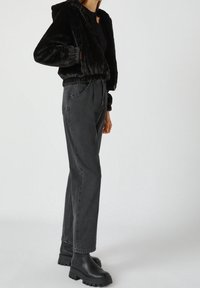 Veste courte en fausse fourrure noire à capuche, associée �à un jean taille haute gris foncé à jambes droites et des bottines noires épaisses.