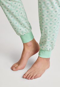 Grüne Jogginghosen mit floralem Muster und gerippten Minz-Bündchen, die aus einem weichen Stoff bestehen. Barfuß sichtbar, was die lässige Passform unterstreicht.