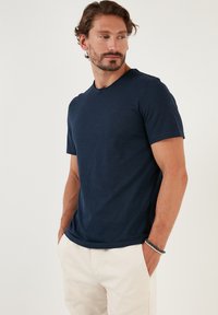 Tricou navy blue cu guler rotund, fabricat dintr-un material moale și texturat, cu mâneci scurte și o croială lejeră, asociat cu pantaloni de culoare deschisă.