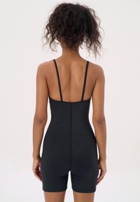 Zwarte bodysuit met dunne banden, aansluitend ontwerp en een gladde textuur. Het heeft een hoge achterkant en korte benen, waardoor een gestroomlijnd silhouet wordt benadrukt.