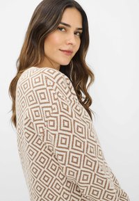 Maglione lavorato a maglia con un motivo geometrico a diamante in beige e marrone. Texture morbida con una vestibilità comoda e polsini a costine.