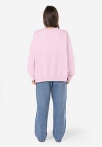 Felpa oversized rosa chiaro con collo a costine e maniche con polsini, abbinata a jeans in denim blu larghi.