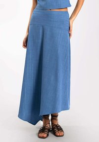 Maxifalda azul, fluida, con un dobladillo asimétrico, confeccionada en una tela ligera con una textura sutil y una cinturilla ajustada.