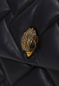 Svart läderväska med quiltad textur. Har en fågelformad låsning i guldfärg med intrikat detaljering och infattade stenar.