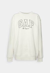 Felpa color crema con collo a giro, che presenta un grande logo "GAP" in nero e il testo "The Original" sotto in un font più piccolo.