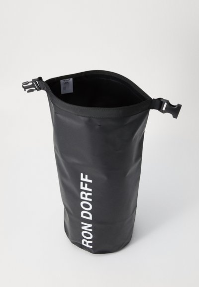 Must beebi kilekott, millel on silindriline kuju, millel on valge trükitud logo, pealmine lukustus klambriga ja reljeefne pind.