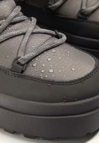 Vodootporne sive čizme s teksturiranom tkaninom, kontrastnom crnom gumom na potplatu i detaljnom vezicom. Kapi vode vidljive na površini.