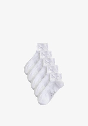 Fünf Paar weiße Knöchelsocken mit gerippter Textur und kleinen dekorativen Schleifen an den Bündchen, fächerförmig angeordnet.