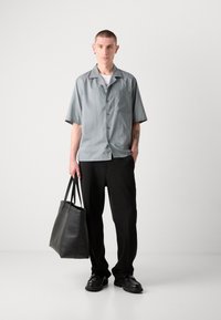 Camisa de botones de manga corta gris claro, pantalones negros y bolsa de piel negra. Textura suave, diseño minimalista, ajuste casual.