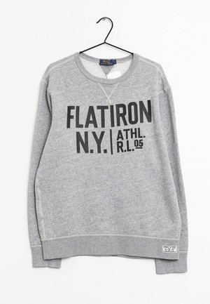 Szara bluza z długim rękawem z nadrukiem "FLATIRON N.Y. ATHL. R.L. 05" w czarnym kolorze, zawieszona na czarnym wieszaku na białym tle.