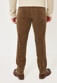 Brown corduroy pants with a ribbed texture, featuring two back pockets, a straight leg design, and brown leather shoes visible.