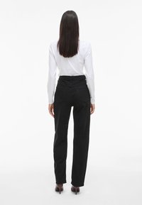 Crne traperice visokog struka ravnog kroja, s dva stražnja džepa i suptilnim detaljima šivanja, u kombinaciji s bijelim majicom dugih rukava.