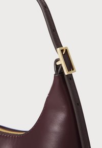 Geantă de mână din piele burgundy cu un finisaj neted, având un accent hardware rectangular de culoare aurie și cusături contrastante închis la curea.