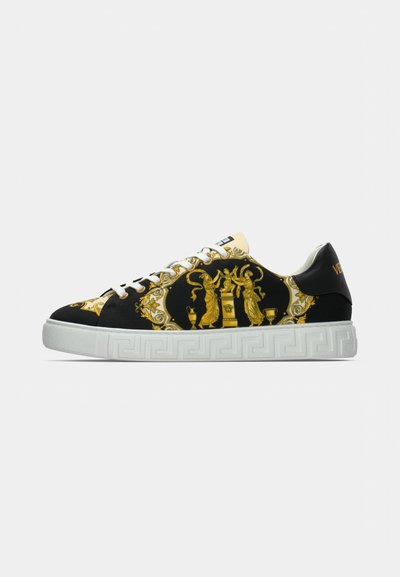 Black sneaker with ornate gold patterns, white rubber sole featuring a Greek key design, and white laces. Accents include a gold logo at the heel.