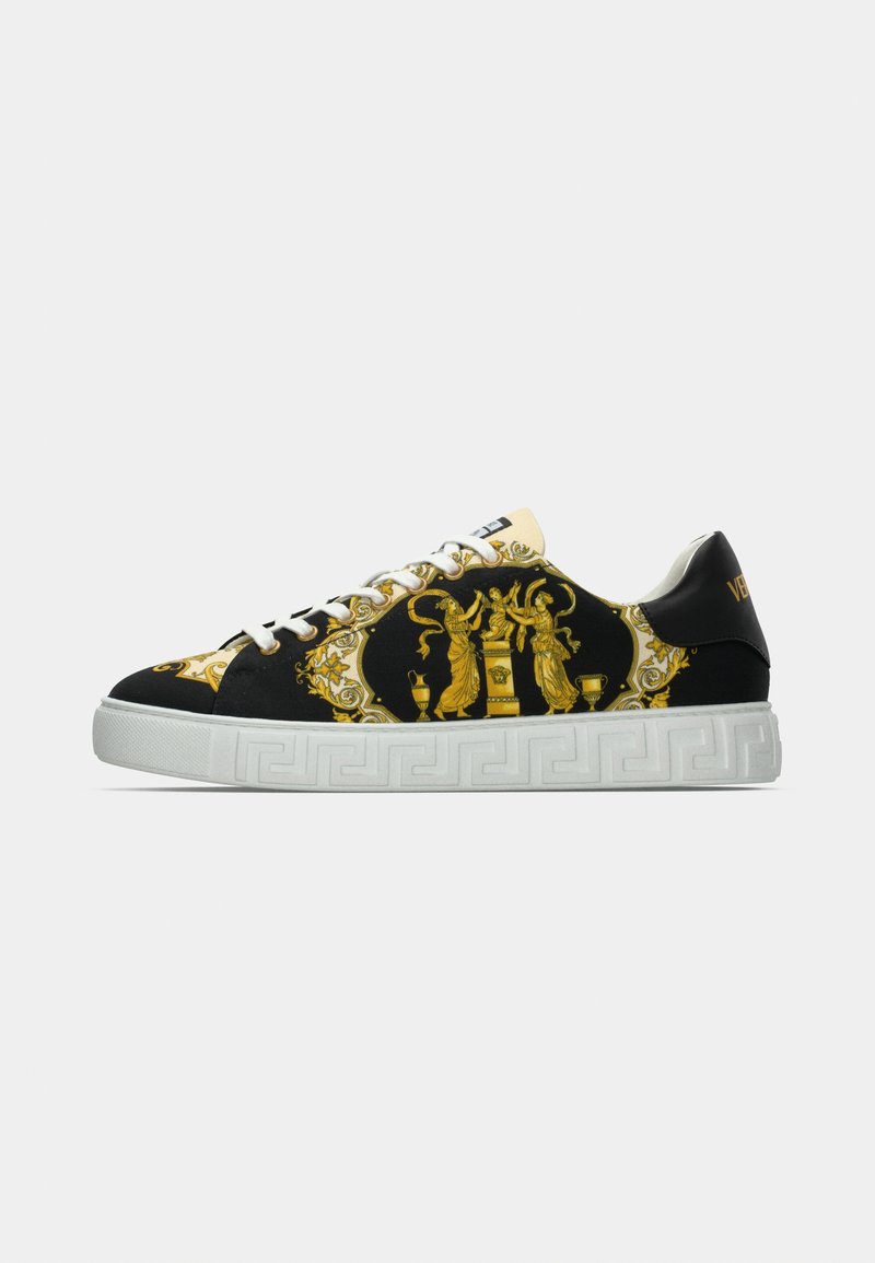 Zwarte sneaker met sierlijke gouden patronen, witte rubberen zool met een Grieks sleutelontwerp en witte veters. Accenten omvatten een gouden logo bij de hiel.