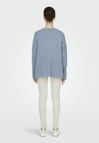 Maglione oversize azzurro chiaro con maniche lunghe, scollo rotondo e orlo a coste, abbinato a pantaloni skinny bianchi e scarpe color crema.