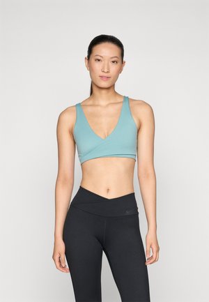 Light blue sports bra with a v-neck design and wide straps, paired with high-waisted black leggings featuring a small logo.
